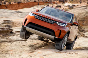橙色 Land Rover Discovery 在岩石沙漠地形上行駛。 — MacBook Pro 壁紙