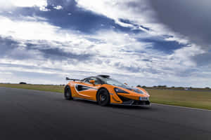 橙色McLaren賽車在多雲天空下在賽道上飛馳 — Surface Pro 壁紙