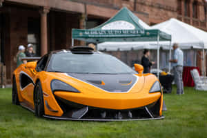 橙色McLaren跑車停在汽車博物館活動的草地上。 — Surface Pro 壁紙