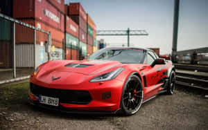 紅色Corvette跑車停在貨櫃和鐵路軌道附近。 — Steam Deck 壁紙