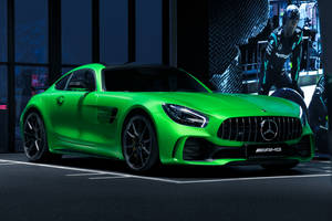 在黑暗的工作室中，一輛充滿活力的綠色Mercedes-AMG GT跑車與一位穿著賽車裝備的技師。 — 綠色動態圖 壁紙