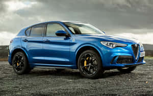 藍色 Alfa Romeo SUV 停泊在碎石地上，背景為多雲天空。 — MacBook Pro 13 壁紙