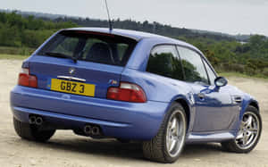 藍色BMW M3跑車停在碎石上，後面有綠色山丘。 — MacBook Pro M1 壁紙