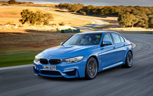 藍色BMW M3轎車在陽光明媚的鄉村蜿蜒道路上飛馳。 — 汽車 壁紙