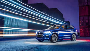 藍色BMW X3 SUV夜間停車，城市工業環境中帶有霓虹光跡。 — 平治 C300 壁紙