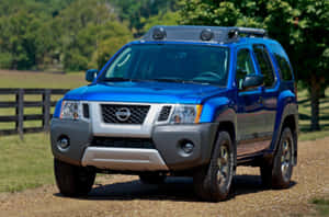 藍色日產Xterra SUV停在碎石路上，靠近木柵欄和綠樹。 — Surface Laptop 壁紙