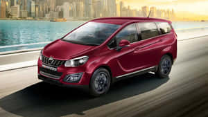 紅色 Marazzo 小型貨車在日落時分於城市附近的海岸高速公路上行駛。 — 高對比 壁紙