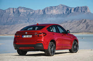 紅色BMW X4 SUV停在沙漠湖床上，背景有山脈。 — Surface Laptop 壁紙