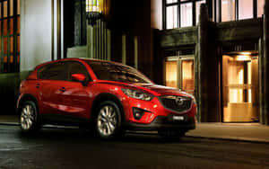 紅色Mazda CX-5 SUV夜間停泊在城市的街道上，靠近有燈光的建築入口。 — Steam Deck 壁紙