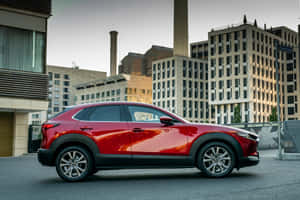 黃昏時停泊在城市街道上的紅色Mazda CX-30 SUV，背景有建築物。 — Surface Laptop 壁紙