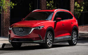 紅色Mazda CX-9 SUV停泊在城市街道上，靠近磚造建築。 — Steam Deck OLED 壁紙