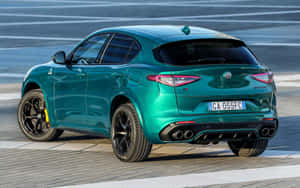青綠色Alfa Romeo Stelvio Quadrifoglio SUV配黑色輪圈和四出排氣管停泊在路面上。 — Steam Deck OLED 壁紙