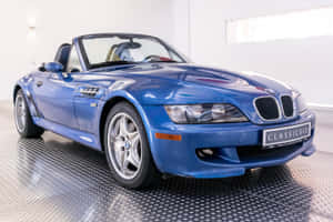 藍色BMW Z3開篷車在潔淨白色車庫內，地板為鑽石紋。 — Surface Laptop 壁紙
