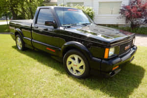 黑色GMC Syclone皮卡車在陽光明媚的日子停放在屋前草地上。 — MacBook Air 13 壁紙