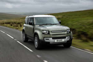 綠色 Land Rover Defender 在鄉村道路上行駛，背景是起伏的山丘。 — Surface Pro 壁紙