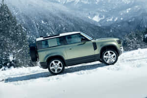 綠色Land Rover Defender在積雪的山路上，旁邊有松樹。 — MacBook Pro 14 壁紙