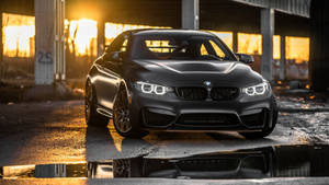 啞光黑色BMW M4停在夕陽下，帶有水坑倒影。 — 汽車 壁紙
