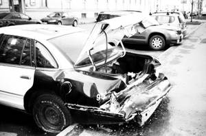 損壞的汽車，車尾被壓碎，後備箱打開，停在潮濕的城市街道上。 — 黑白 壁紙