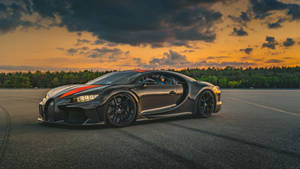 日落時分賽道上的黑色Bugatti Chiron，帶有橙色點綴和森林背景。 — 汽車 壁紙