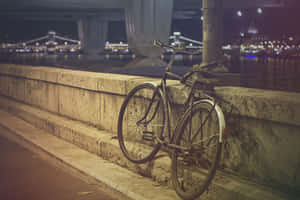 夜晚河邊石欄杆旁靠著一輛單車，背景有亮燈的橋樑。 — MacBook Air M3 壁紙