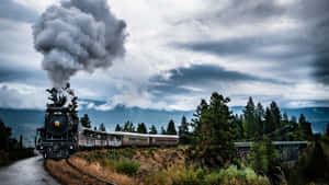 一輛黑色蒸汽火車在多雲天空下穿過森林覆蓋的山地景觀，排放煙霧。 — 霍格華茲 GIF 壁紙