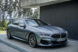 啞光灰色BMW 8系停在現代混凝土結構下，背景有樹木。 — MacBook 壁紙