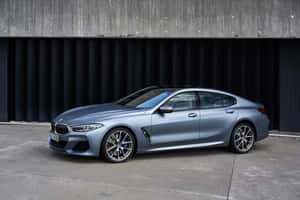 啞光藍色BMW 8系轎跑車停靠在混凝土和金屬牆邊。 — Surface Pro 壁紙