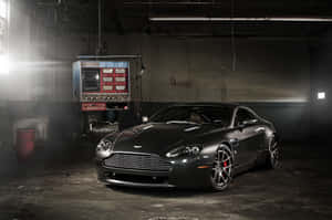昏暗工業車庫中聚光燈下的啞光黑色Aston Martin。 — Surface Pro 壁紙
