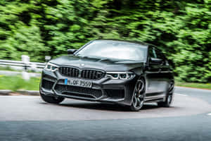 啞光黑色BMW M5在森林道路上高速行駛，背景有模糊的綠樹。 — 酷車 壁紙