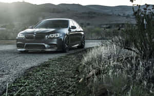 啞光黑色BMW M5停在碎石路上，附近有乾草和山丘，黃昏時分。 — 1280x800 壁紙