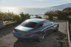 時尚的藍色 Genesis X 汽車停泊在懸崖上，俯瞰夕陽下的海洋。 — Surface Laptop 壁紙