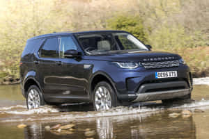 深藍色 Land Rover Discovery 在淺河水中行駛。 — Surface Pro 壁紙