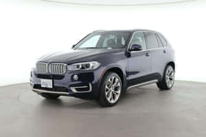 一輛深藍色BMW X5 SUV在乾淨的工作室環境中，配有白色牆壁和灰色地板。 — MacBook Pro M3 壁紙