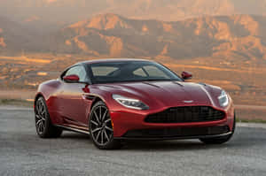 紅色Aston Martin跑車停在碎石路上，背景是日落時分的山脈。 — Surface Pro 壁紙