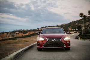 紅色Lexus轎車在黃昏時分行駛於海岸道路，背景有棕櫚樹和山丘。 — MacBook Air M4 壁紙