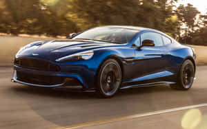藍色 Aston Martin 在日落時分的道路上奔馳，背景有樹木。 — Steam Deck 壁紙