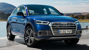 藍色 Audi Q5 SUV 停在湖邊，背景有山脈。 — 奧迪 GIF 壁紙