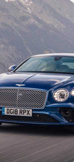 藍色 Bentley Continental GT 在白雪覆蓋的山路上飛馳。 — Samsung S23 壁紙