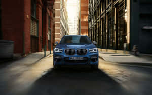 藍色BMW SUV行駛在磚砌和玻璃建築之間陽光普照的城市小巷中。 — Steam Deck OLED 壁紙