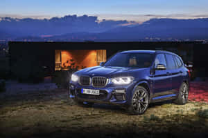 藍色BMW X3 SUV在黃昏時停在一棟帶有明亮窗戶的現代房屋附近。 — Surface Laptop 壁紙