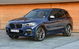 藍色BMW X3 SUV停放在木車庫前，拋光合金輪圈。 — Steam Deck OLED 壁紙
