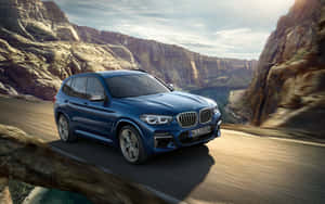 藍色BMW X3 SUV在峽谷道路上行駛，背景有懸崖和河流。 — Steam Deck OLED 壁紙