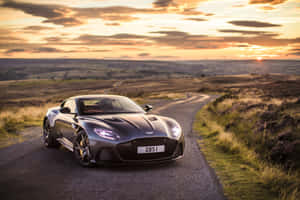 日落時分蜿蜒鄉村道路上的銀色Aston Martin DBS1。 — Surface Pro 壁紙