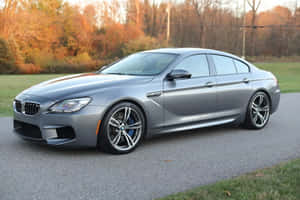 銀色BMW M6跑車停在碎石上，背景有秋樹。 — MacBook Air M3 壁紙