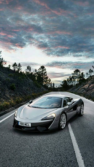 銀色McLaren跑車在暮色中的山路上，天空色彩繽紛 — 引擎 壁紙