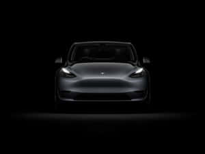 在黑暗工作室中，車頭燈照亮銀色Tesla Model 3的正面視圖。 — Tesla GIF 壁紙
