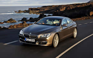 一輛青銅色BMW 6系在日落時分行駛在海岸公路上。 — Steam Deck OLED 壁紙