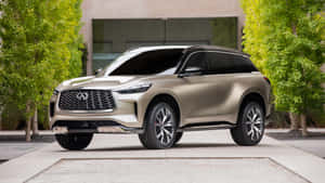 香檳金色Infiniti SUV停在一棟有綠樹的現代化房屋前。 — Studio Display 壁紙