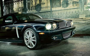 黑色 Jaguar XK8 夜間停在潮濕路面上華麗的鐵門附近。 — Steam Deck 壁紙