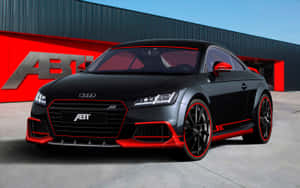 黑色ABT Audi TT跑車帶紅色飾邊，停在紅黑建築前。 — Steam Deck OLED 壁紙
